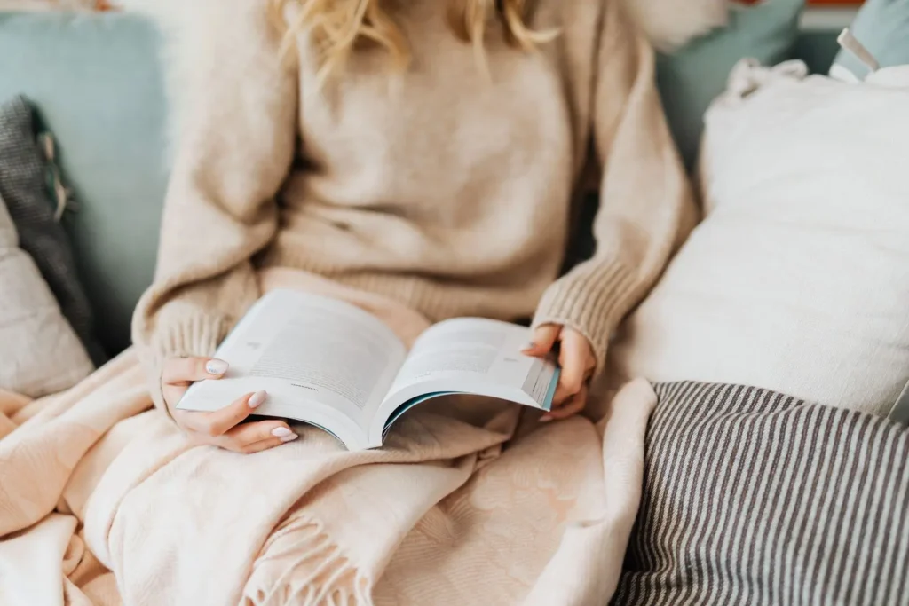 Woman reading on a cozy beige sofa with a blanket — self-care that fits into a real schedule