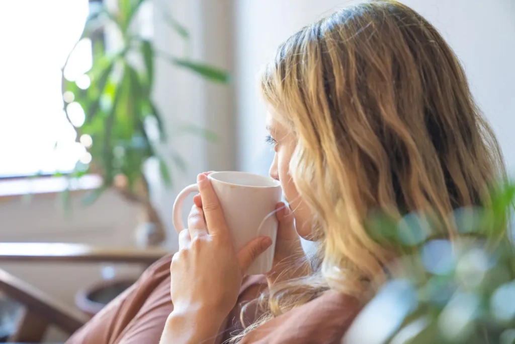 Woman holding a warm pink mug with plants in the background — stress relief habits you can do in 10 minutes