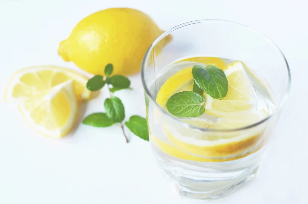 Glass of water with lemon slices and fresh mint in natural light — simple hydration habits that make drinking water easier